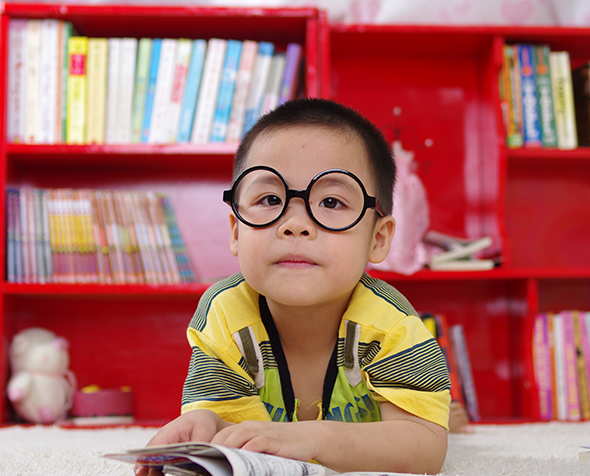 small boy in library reading a book​