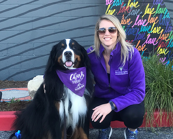 Woman smiling kneeling next to Charles the therapy dog. 