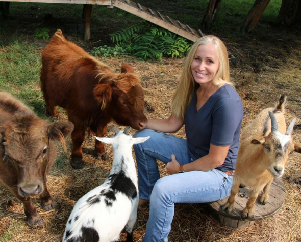 Pamela Wheeler seated outside surrounded by goats and calves.