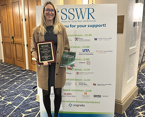 Professor of the Practice Rachel Forbes poses for a photo with her book and award during a conference.