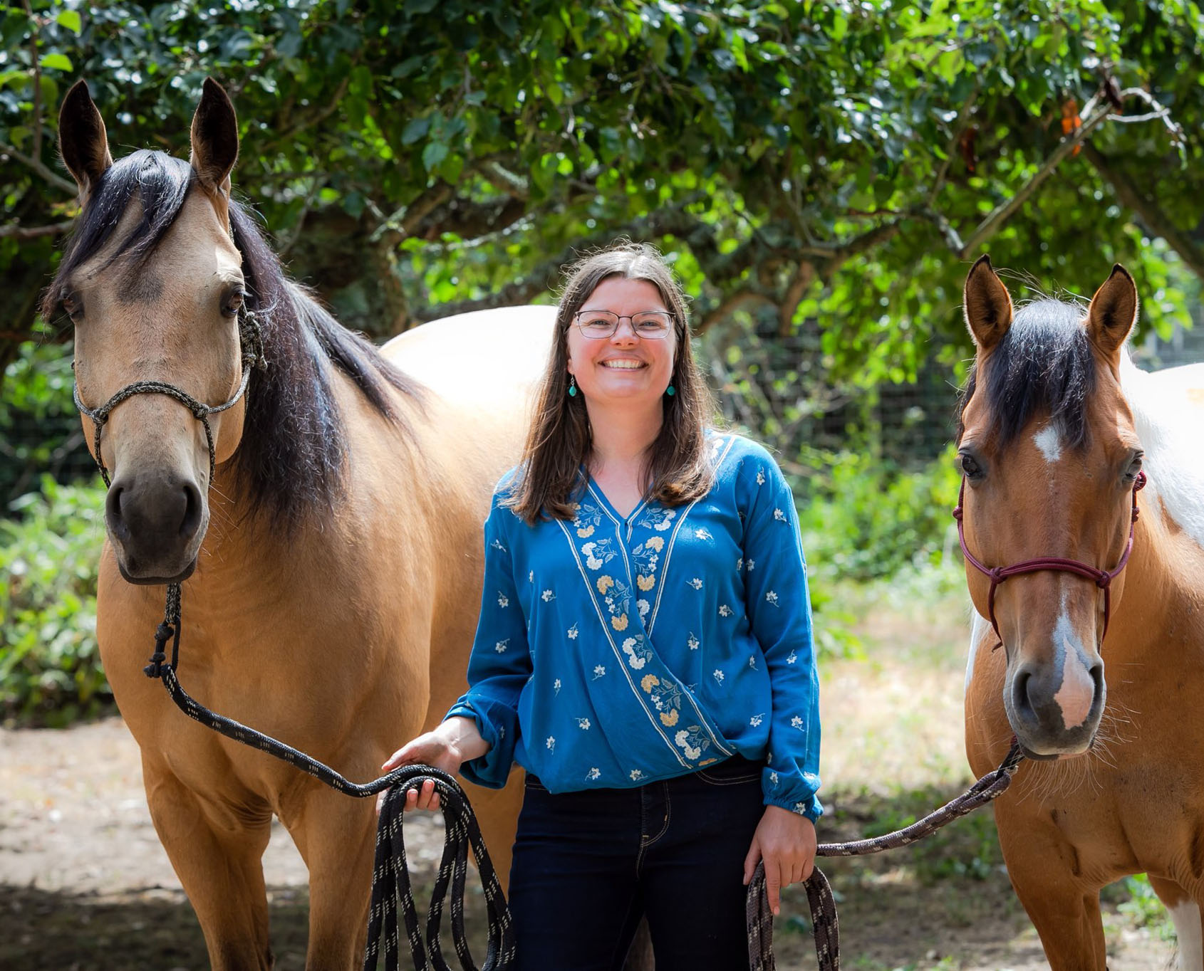 woman smiling and standing between two horses at a therapeutic ranch