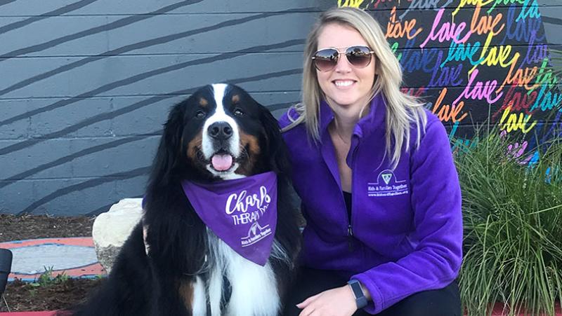 Woman smiling kneeling next to Charles the therapy dog. 