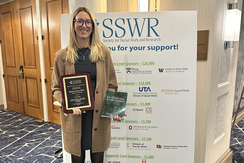 Professor of the Practice Rachel Forbes poses for a photo with her book and award during a conference.