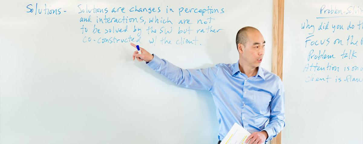 Professor lecturing pointing at the board behind him