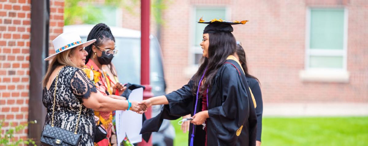 Graduate dressed in regalia shaking hands and greeting other folks