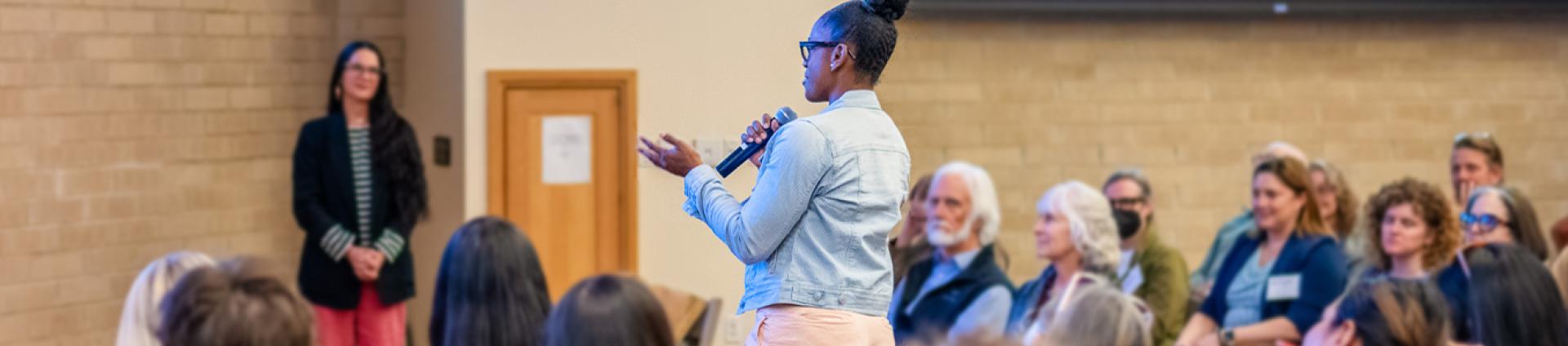 woman standing up asking a question at a community event in Craig Hall