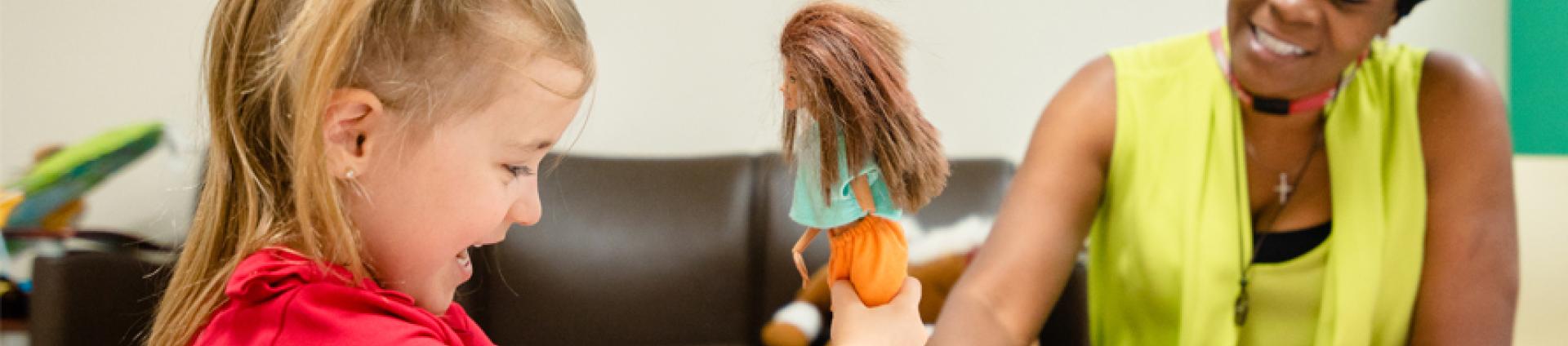 Child playing with doll, woman watching