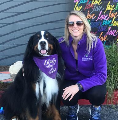 Woman smiling kneeling next to Charles the therapy dog. 